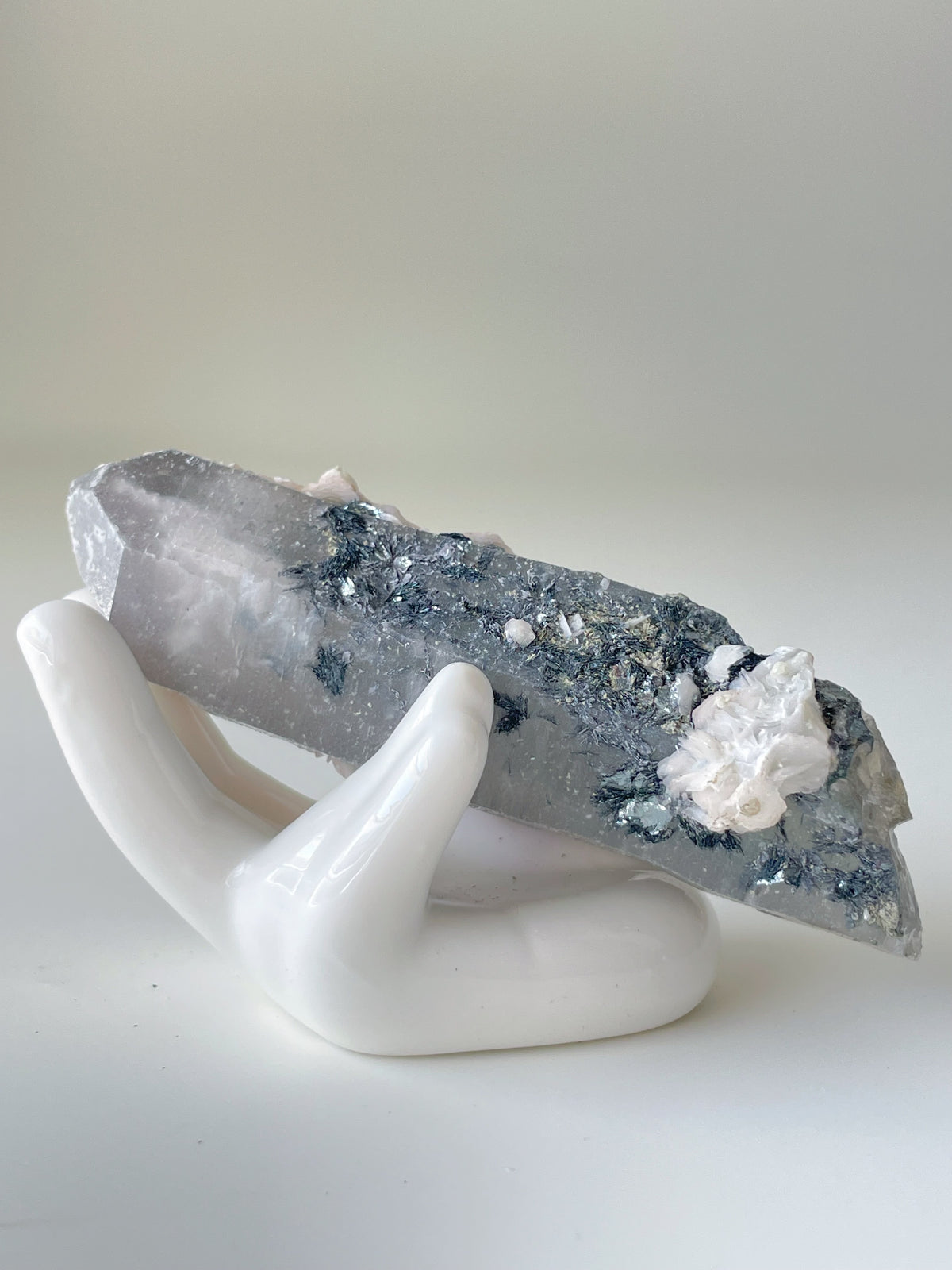 A stunning pink petal calcite specimen resting on a white ceramic hand display, showcasing its unique crystal formations.