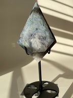 Scenic moss agate crystal specimen displayed on a sleek black stand, showcasing its unique patterns and colors.