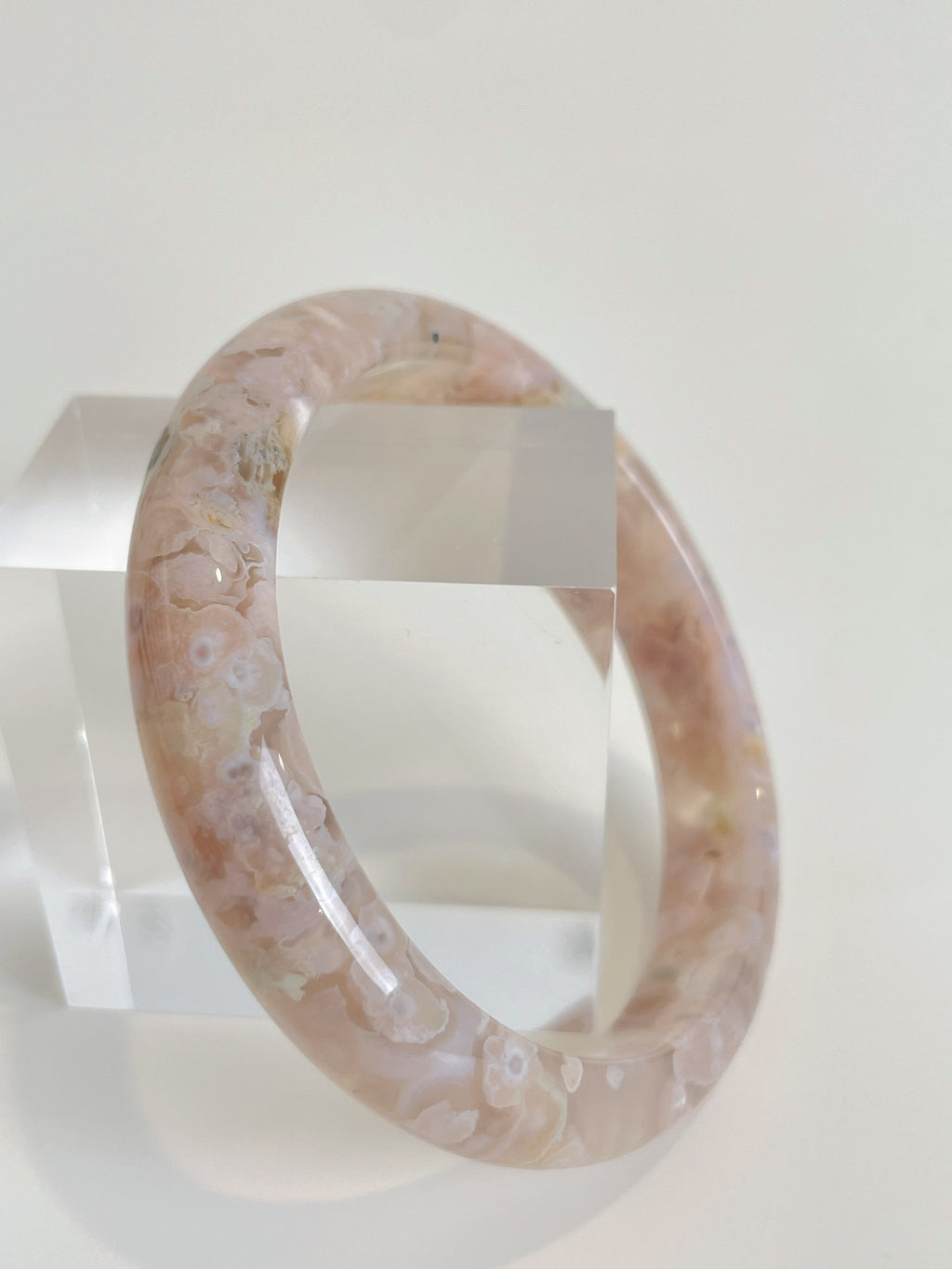 Beautiful flower agate bangle showcasing soft pink hues and floral patterns, displayed beside a clear crystal block.