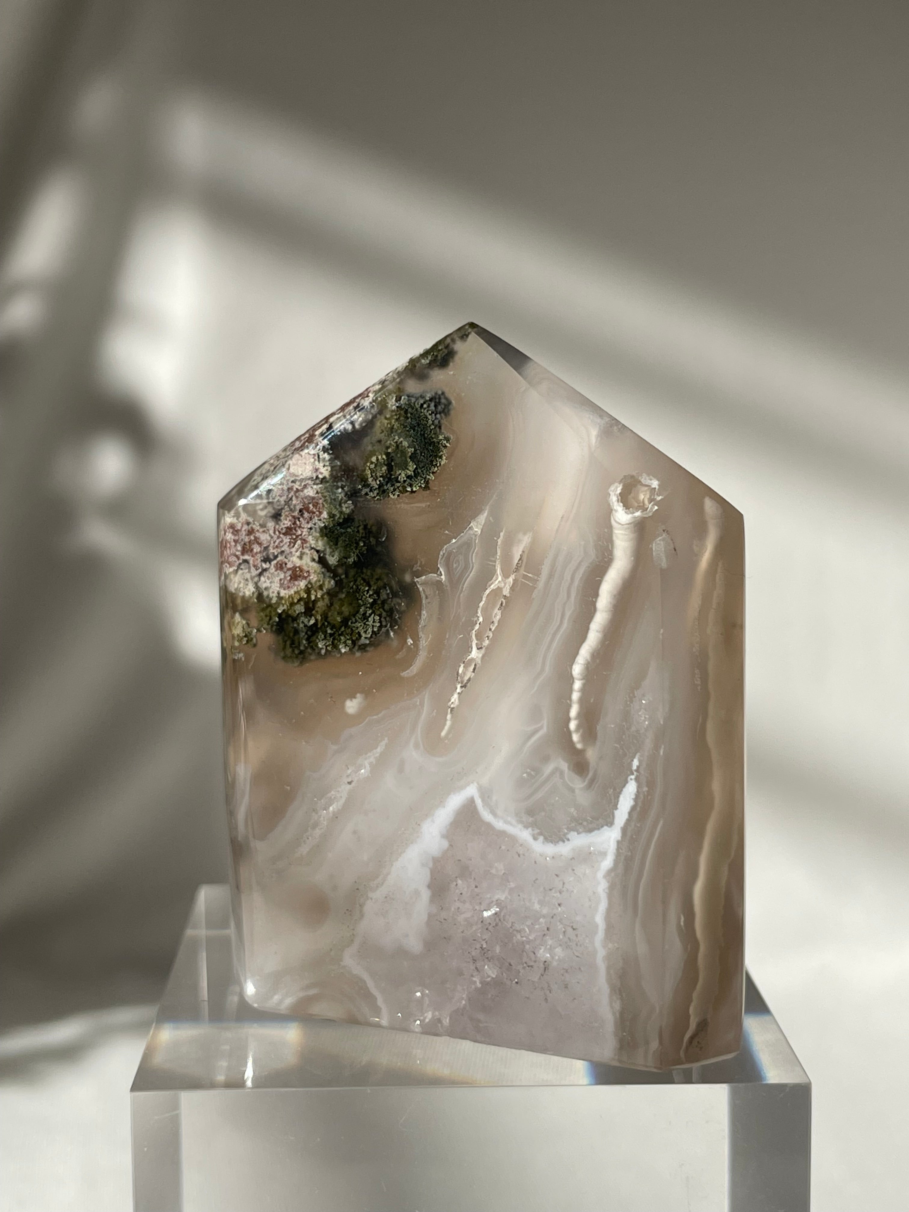 Scenic moss agate tower with earthy tones and unique patterns, displayed on a clear pedestal.