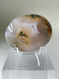 Scenic moss agate palm stone with earthy tones and intricate patterns, displayed on a clear stand.