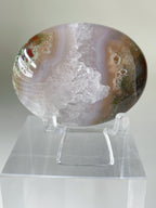 Scenic moss agate palm stone displayed on a clear stand, showcasing its unique patterns and earthy tones.