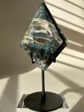 Scenic moss agate specimen displayed on a sleek black stand, showcasing its unique patterns and colors.