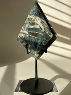Scenic moss agate specimen displayed on a sleek black stand, showcasing its unique patterns and colors.