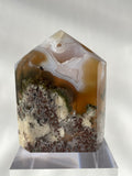 Scenic moss agate tower with earthy tones and intricate patterns, displayed on a clear base.