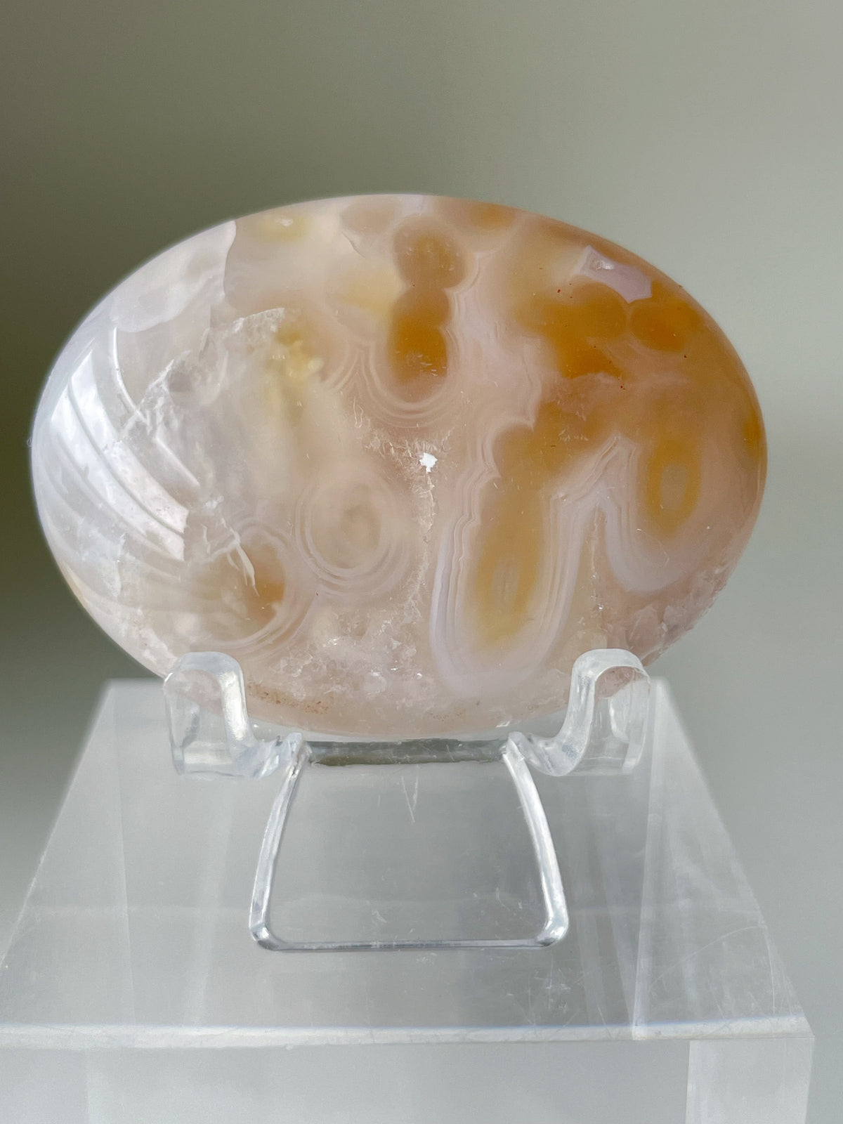 Scenic moss agate palm stone with soft swirls of beige and cream, displayed on a clear stand.