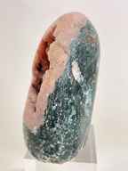 Freeform pink amethyst crystal specimen with green and white accents, displayed on a clear stand.
