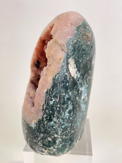 Freeform pink amethyst crystal specimen with green and white accents, displayed on a clear stand.