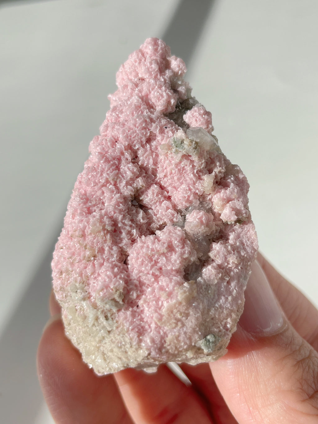 Beautiful rhodochrosite cluster with a pink, textured surface, held in a hand, showcasing its natural beauty.