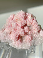 Beautiful rhodochrosite cluster with delicate pink crystals, displayed on a clear stand, showcasing its natural beauty.