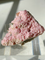 Beautiful rhodochrosite cluster with a pink, textured surface, displayed on a clear stand.