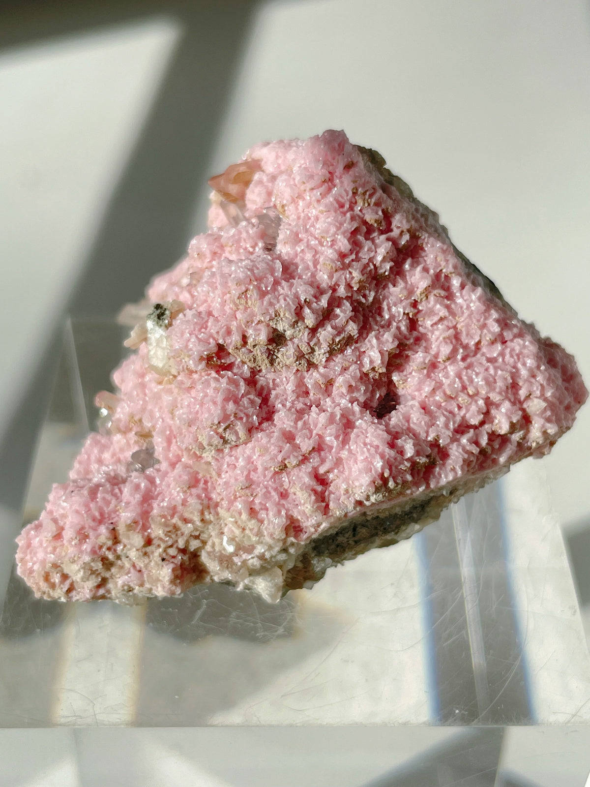 Beautiful rhodochrosite cluster with a pink, textured surface, displayed on a clear stand.