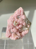 Rhodochrosite cluster with a soft pink hue, showcasing intricate crystal formations on a clear display stand.