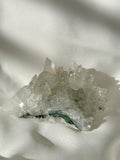 Sparkling apophyllite cluster with clear crystals resting on a soft, light fabric background.