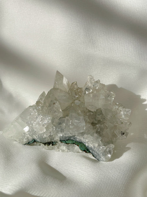 Sparkling apophyllite cluster with clear crystals resting on a soft, light fabric background.
