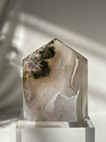 Scenic moss agate crystal tower with earthy tones and natural patterns, beautifully displayed on a clear base.