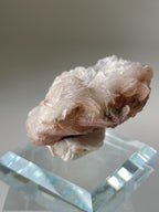 Beautiful pink petal calcite specimen resting on a clear crystal base, showcasing delicate layers and textures.