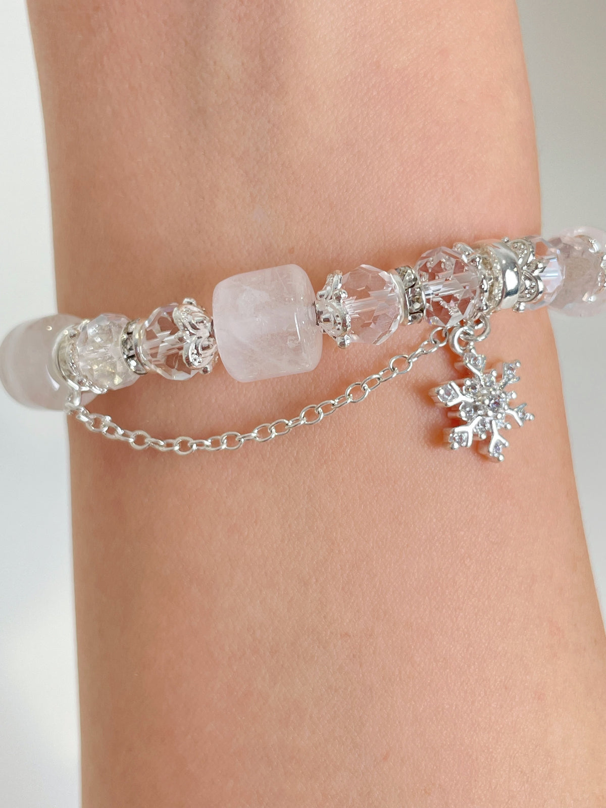 Elegant white quartz bracelet featuring crystal beads and a silver snowflake charm, worn on a wrist.