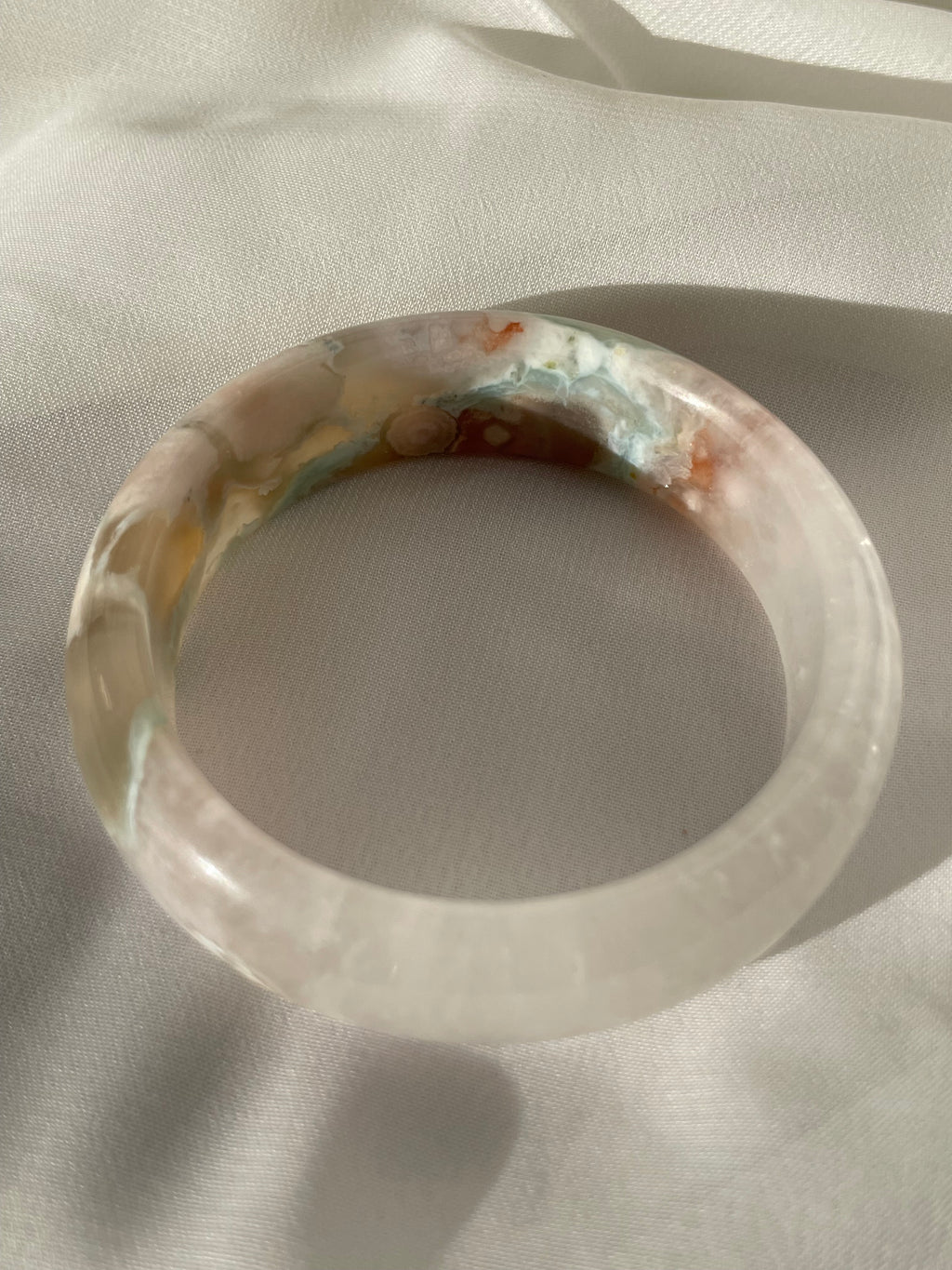 Beautiful flower agate bangle showcasing soft pink and earthy tones, resting on a light fabric background.