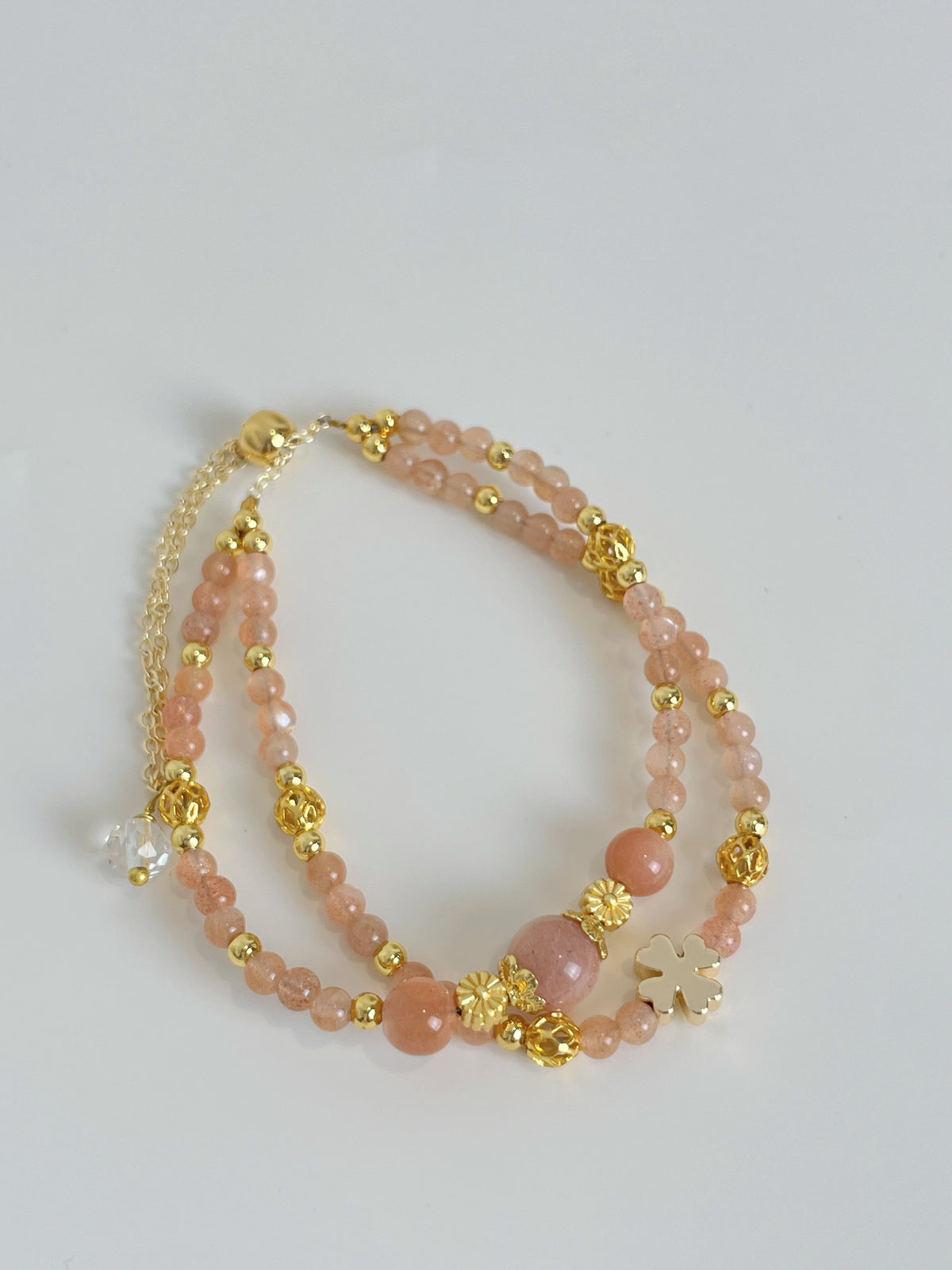Peach moonstone bracelet featuring 3.5mm beads, adorned with gold accents and a floral charm.