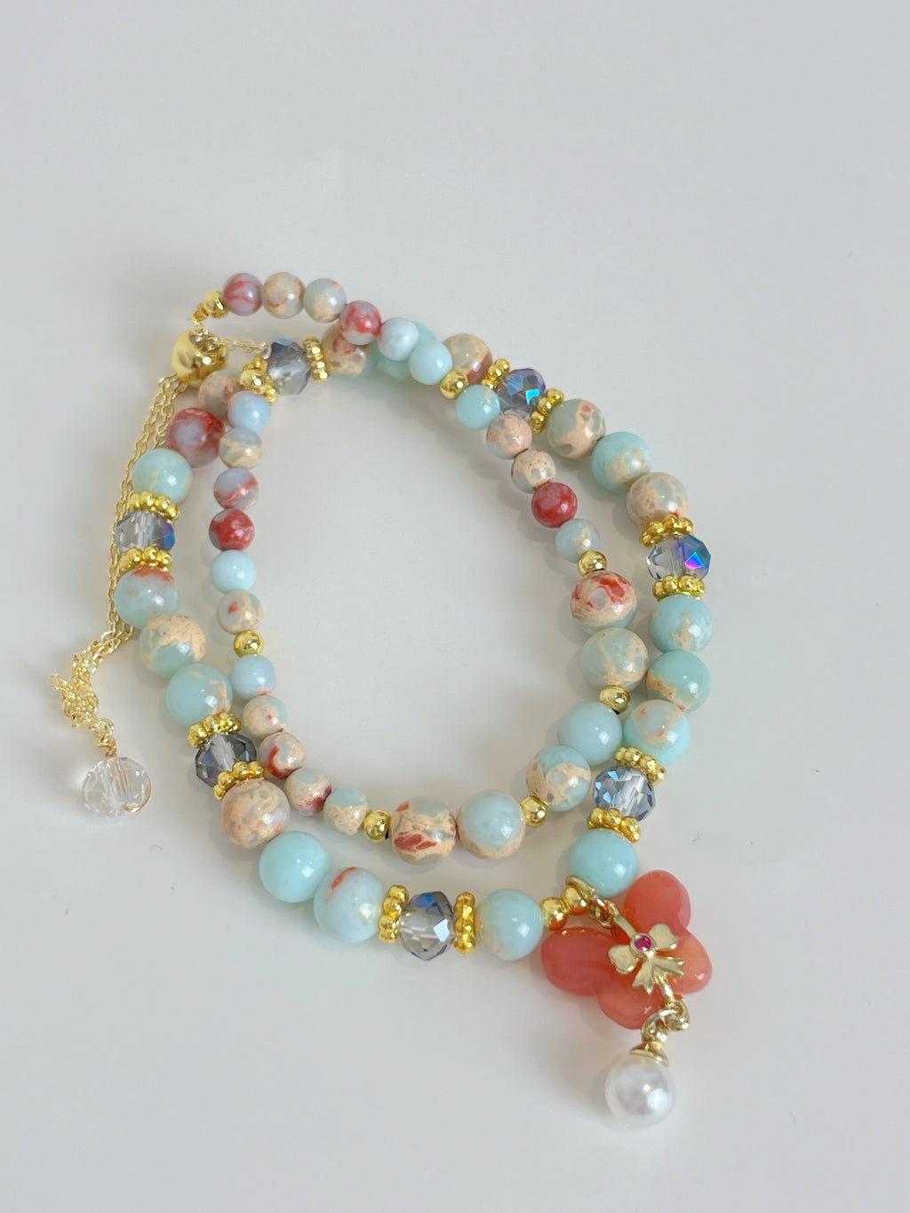 A double bracelet featuring colorful beads, including light blue and coral, accented with gold and crystal details.