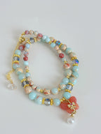 A double bracelet featuring colorful beads, including light blue and coral, accented with gold and crystal details.