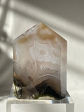 Scenic moss agate tower with unique patterns and earthy tones, resting on a clear base.