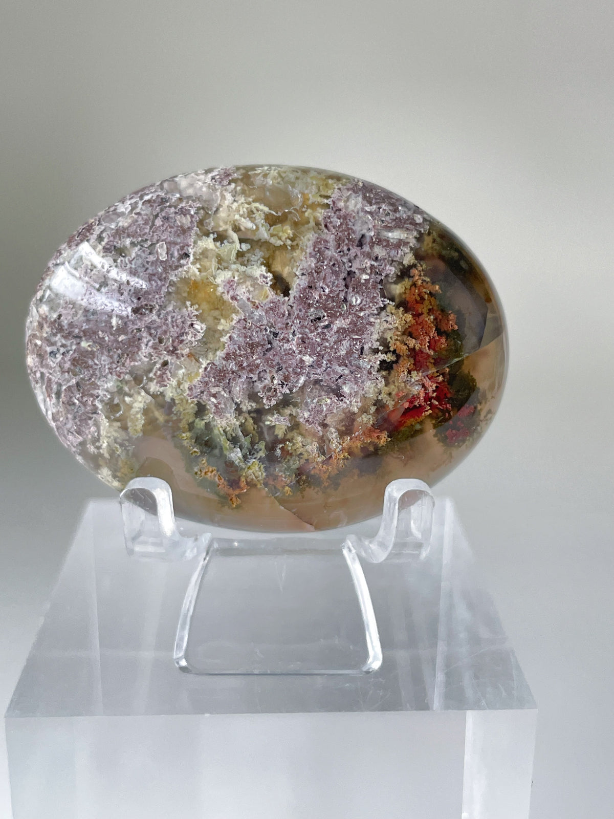 Scenic moss agate palm stone displayed on a clear stand, showcasing earthy tones and intricate patterns.
