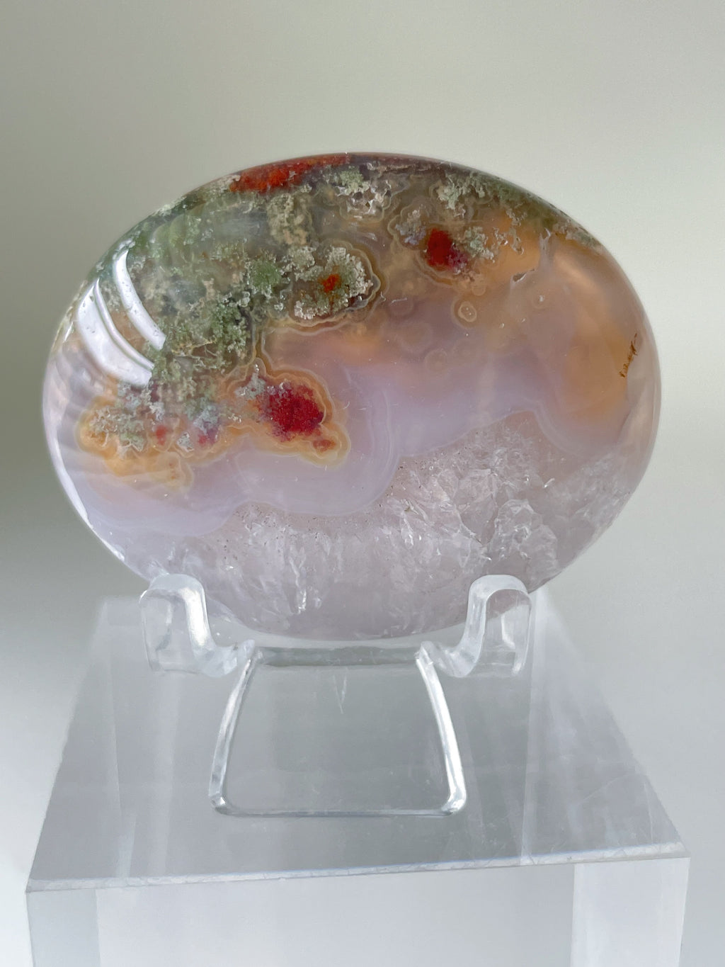 Scenic moss agate palm stone with vibrant colors and patterns, displayed on a clear stand.