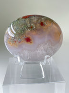 Scenic moss agate palm stone with vibrant colors and patterns, displayed on a clear stand.