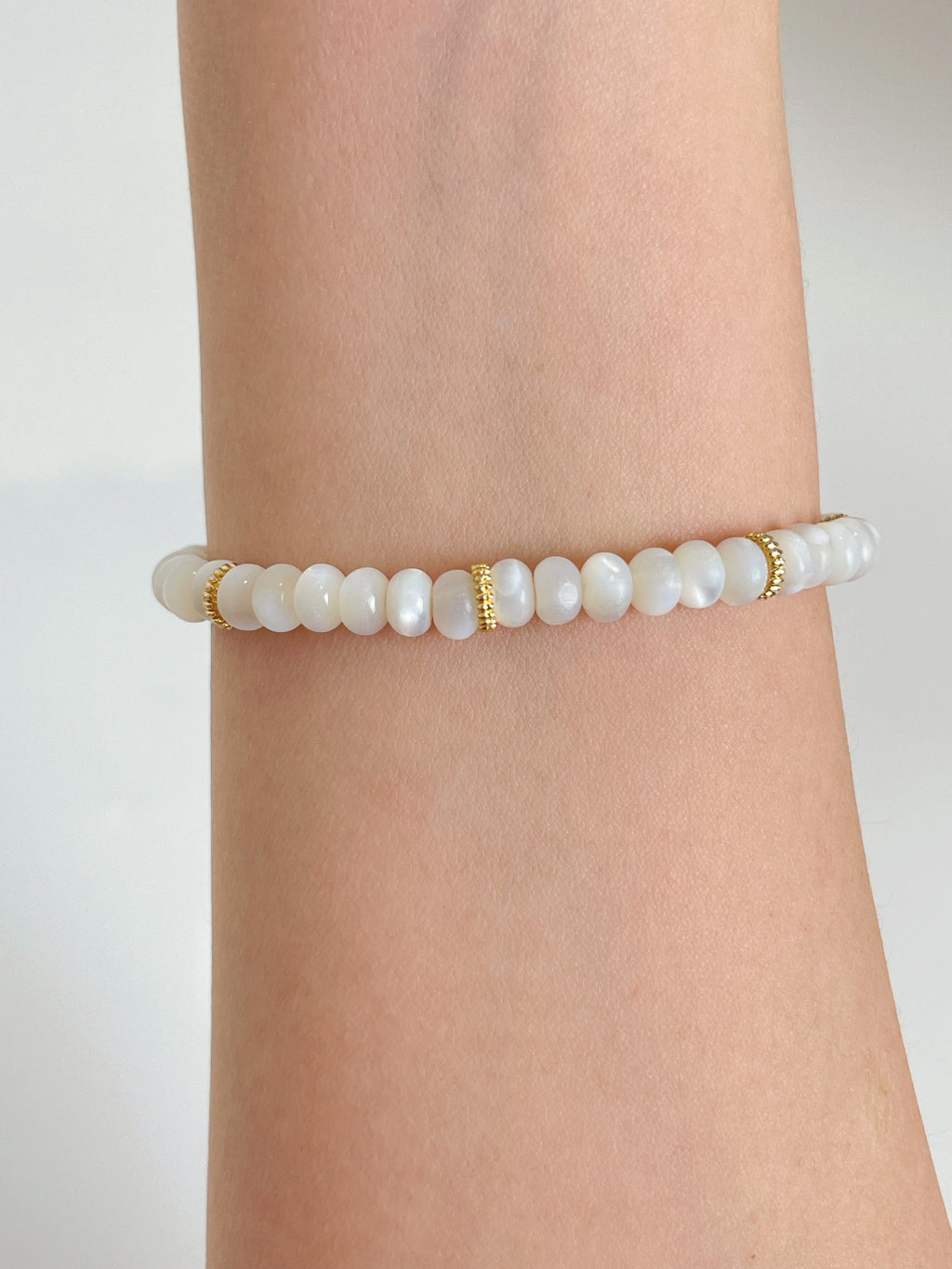 Elegant mother of pearl bracelet featuring smooth beads with gold accents, worn on a wrist.