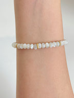 Elegant mother of pearl bracelet featuring smooth beads with gold accents, worn on a wrist.