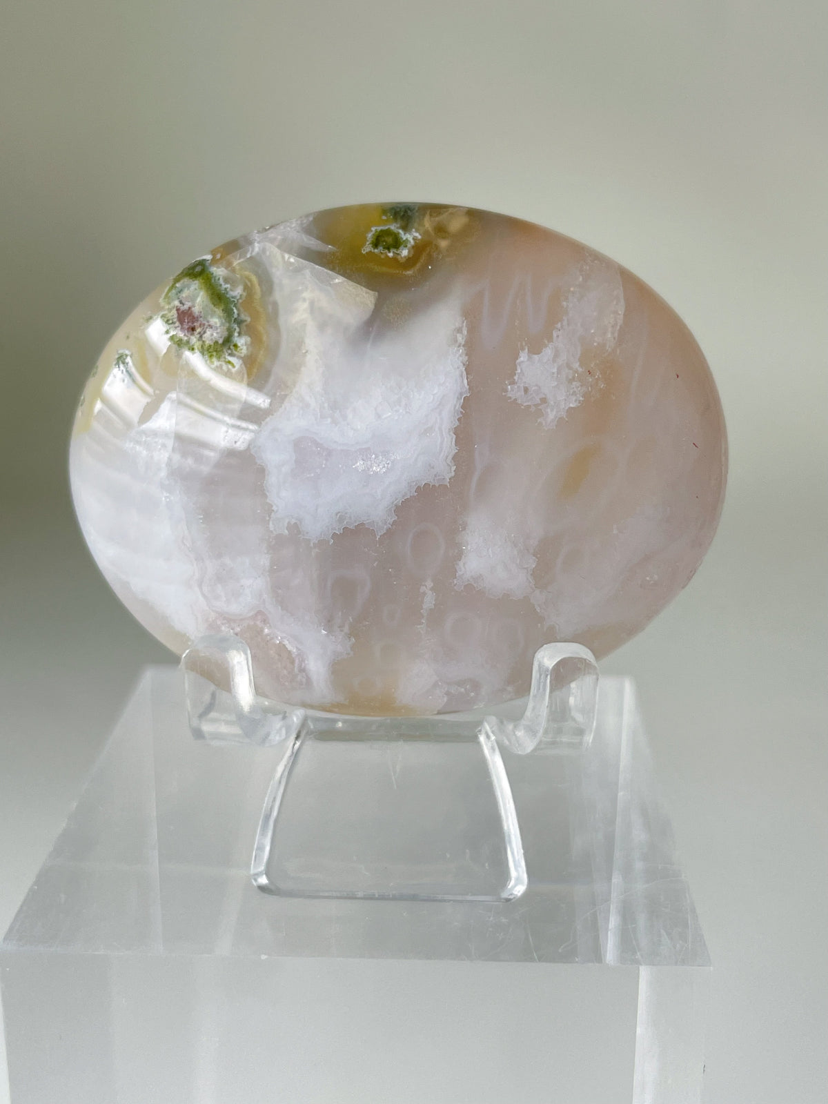 Scenic moss agate palm stone displayed on a clear stand, showcasing its unique patterns and colors.