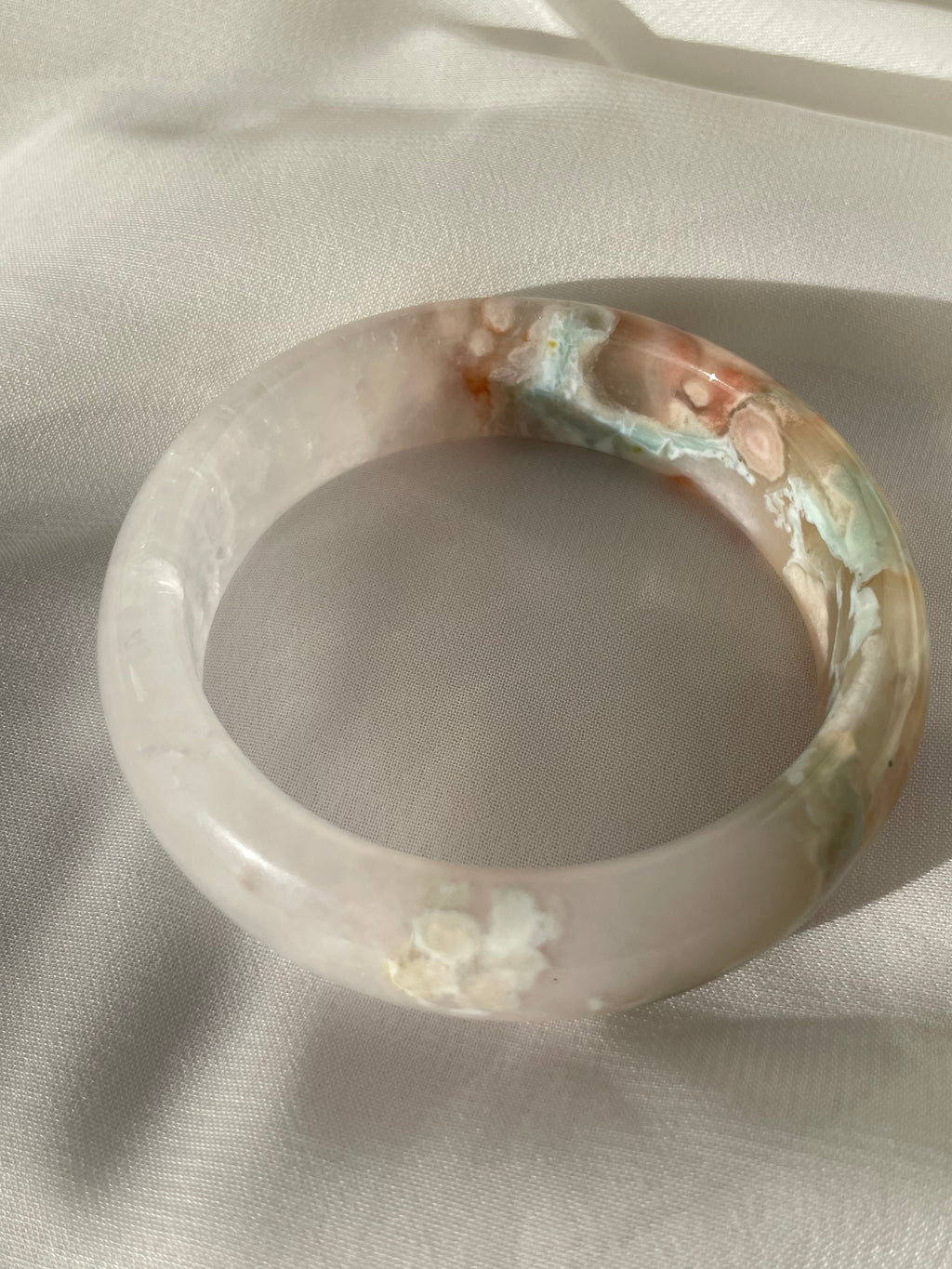 Beautiful flower agate bangle featuring soft pink and blue hues, resting on a light fabric surface.
