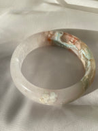 Beautiful flower agate bangle featuring soft pink and blue hues, resting on a light fabric surface.