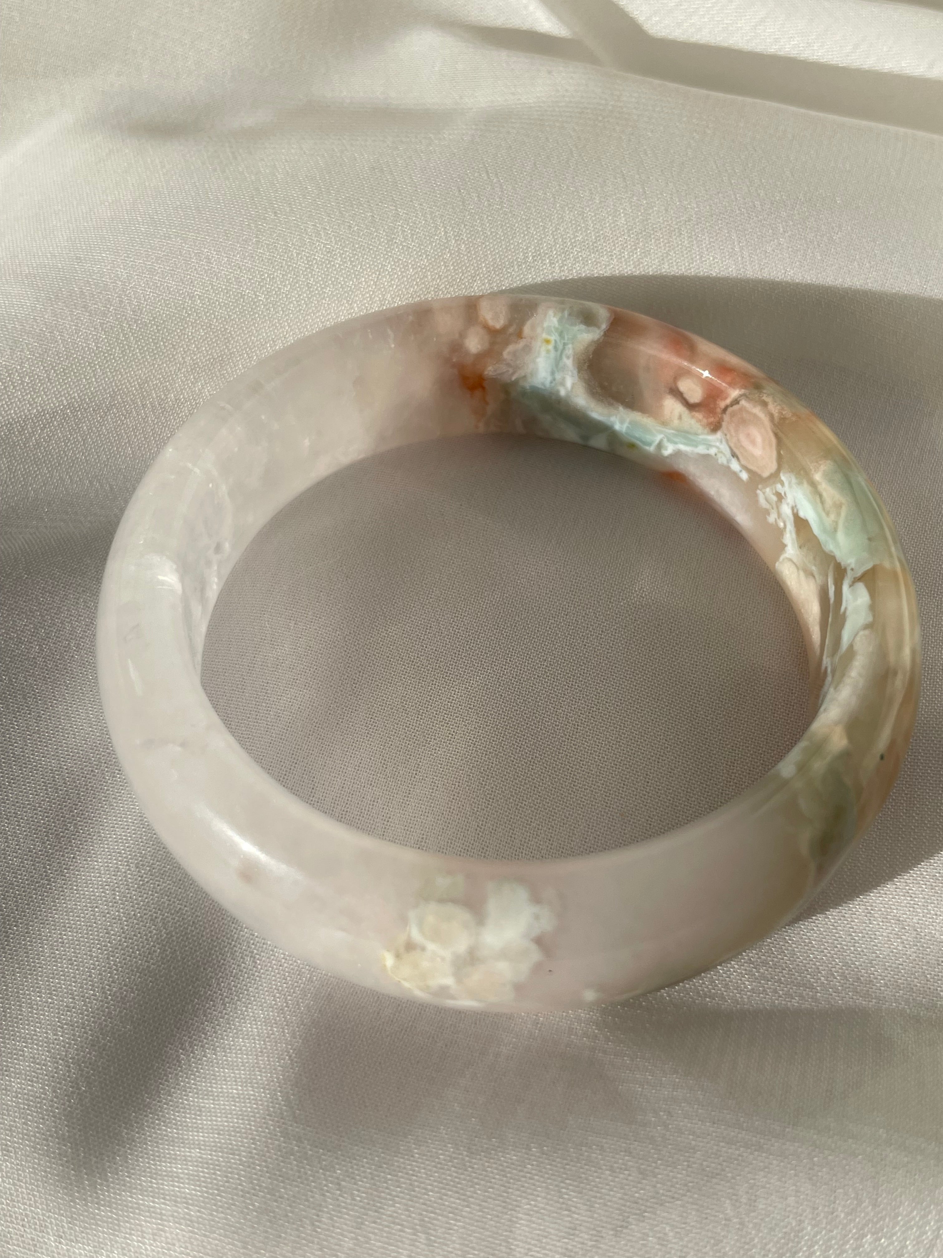Beautiful flower agate bangle featuring soft pink and blue hues, resting on a light fabric surface.