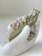 Beautiful rosette petal calcite specimen resting in a white hand sculpture, showcasing intricate floral patterns.