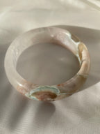 Beautiful flower agate bangle with soft pink and earthy tones, resting on a light fabric background.