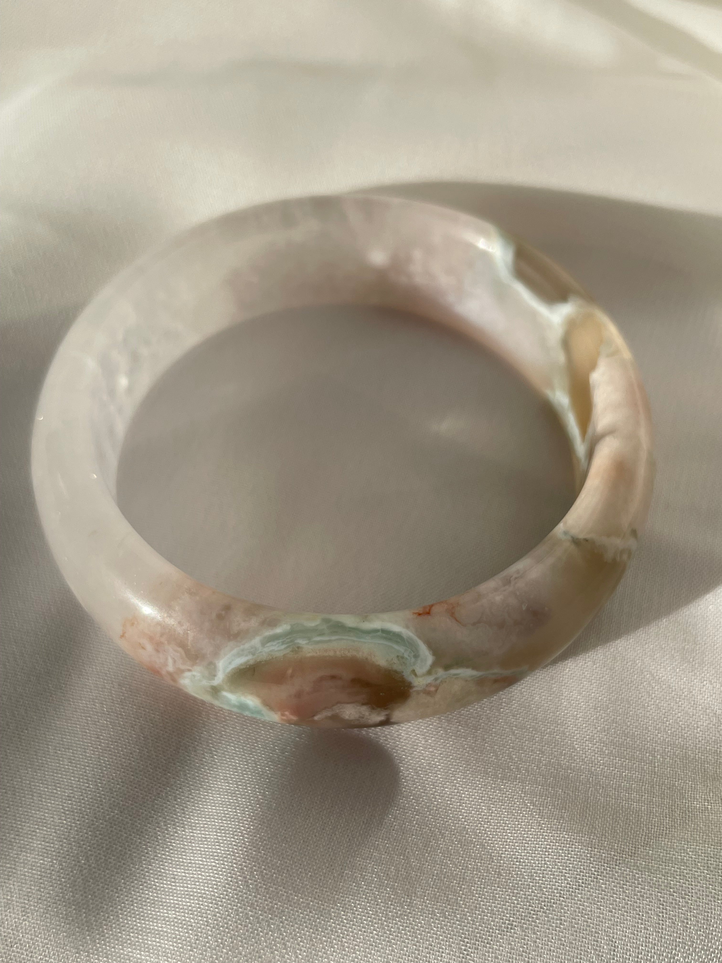 Beautiful flower agate bangle with soft pink and earthy tones, resting on a light fabric background.