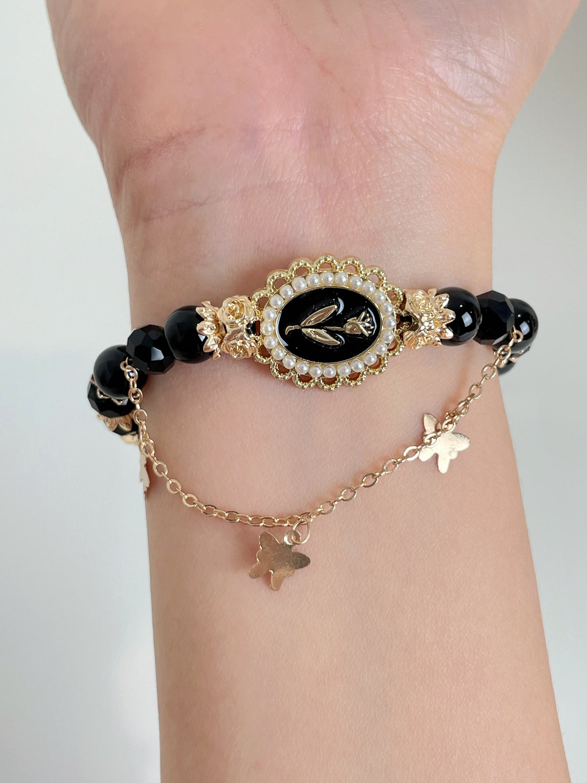 Elegant black obsidian bracelet featuring a decorative centerpiece and delicate butterfly charms.