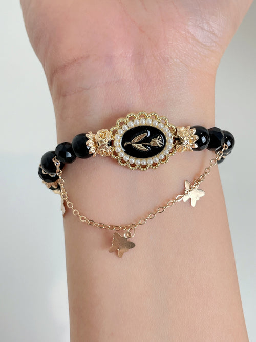 Elegant black obsidian bracelet featuring a decorative centerpiece and delicate butterfly charms.