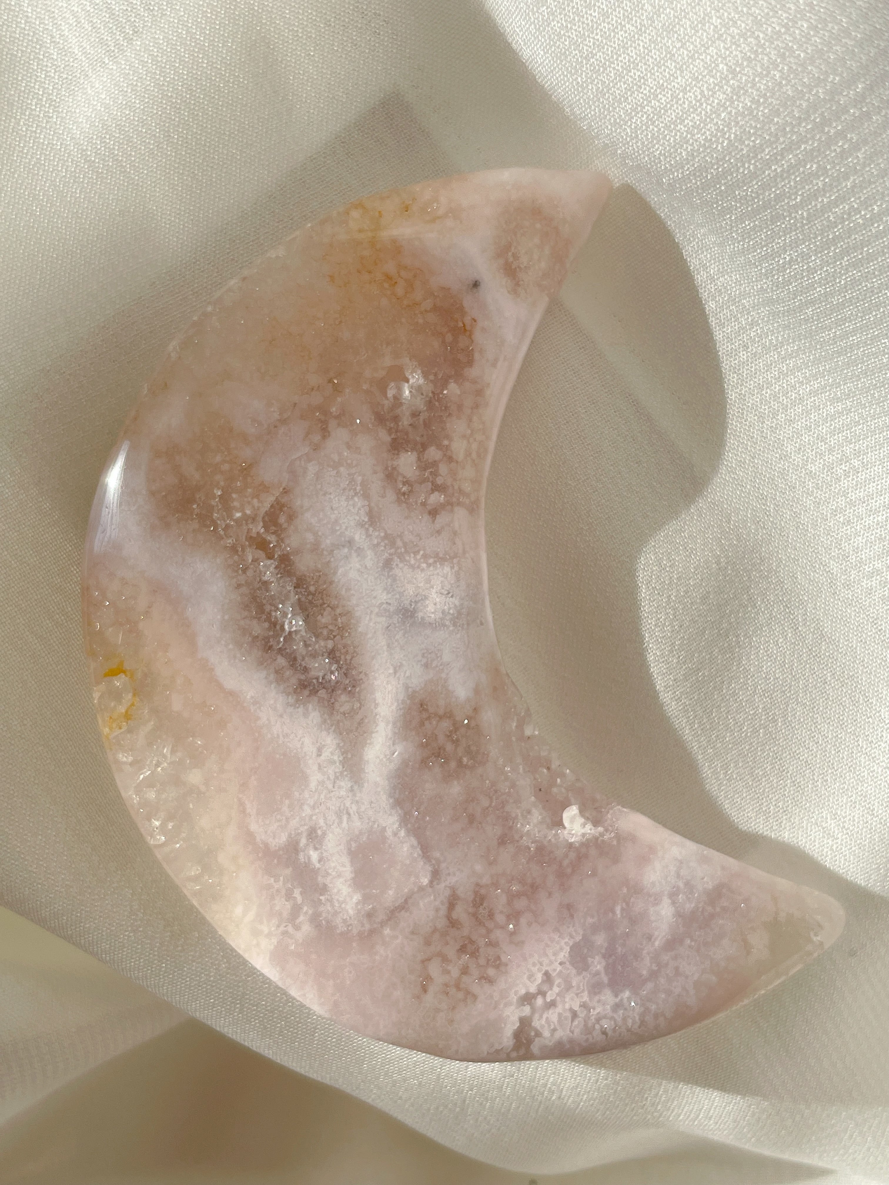 Beautiful flower agate moon with soft pink and earthy tones, resting on a light fabric background.
