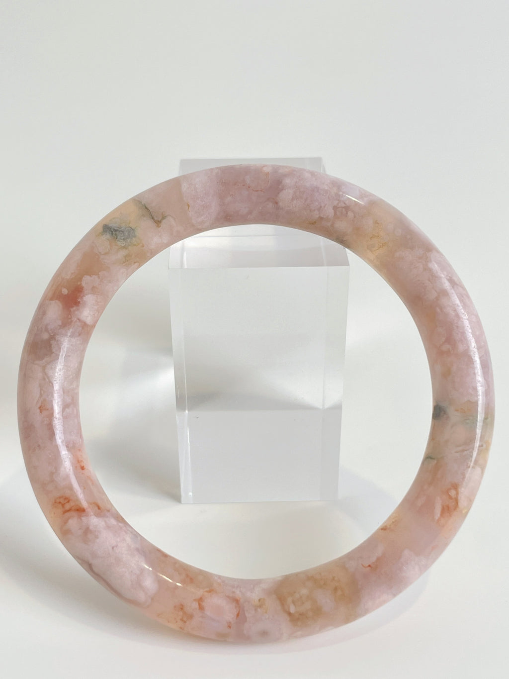 Beautiful flower agate bangle showcasing soft pink hues and natural patterns, displayed beside a clear stand.