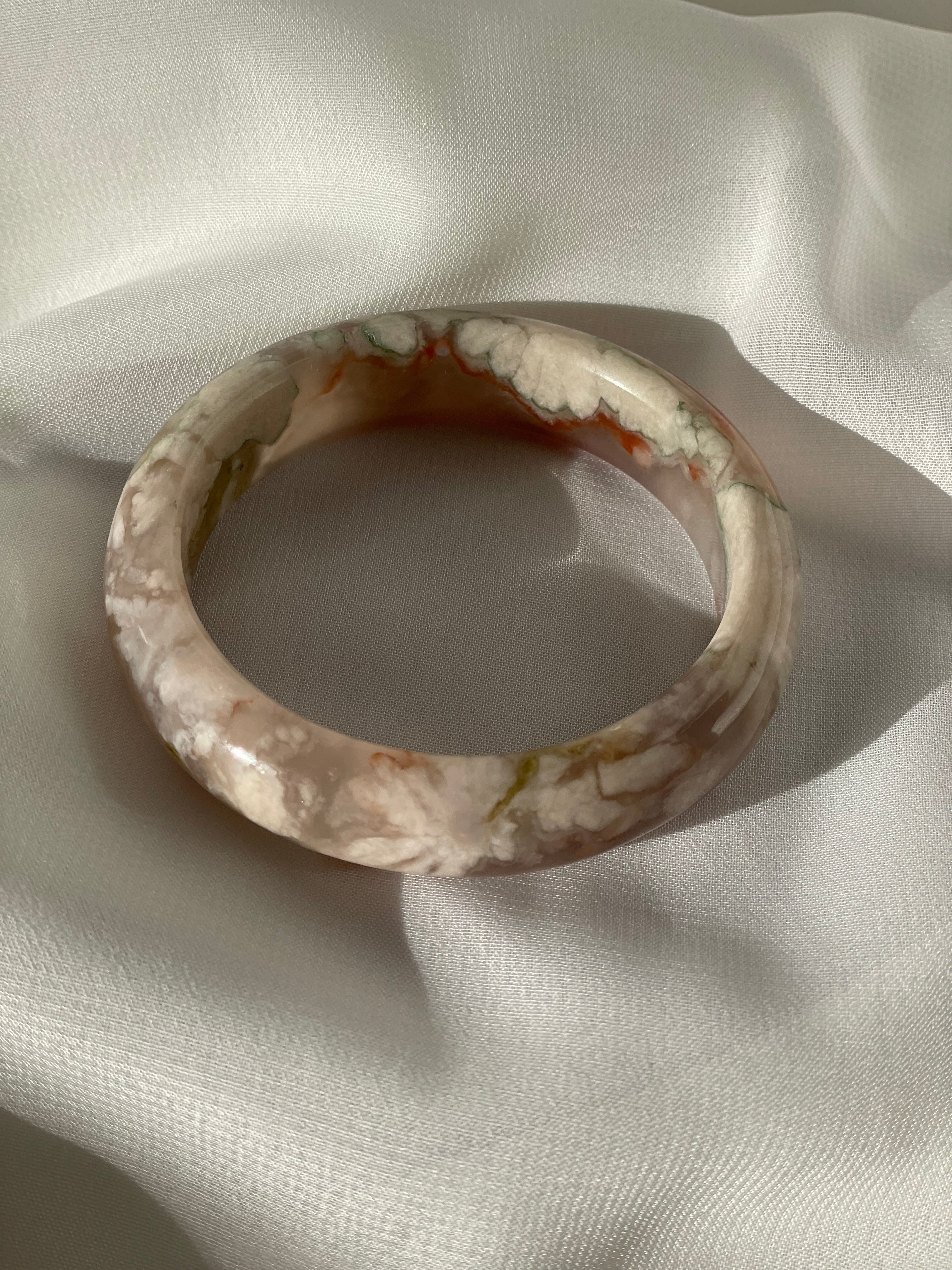 Beautiful flower agate bangle with soft pink and green patterns, resting on a smooth white fabric.