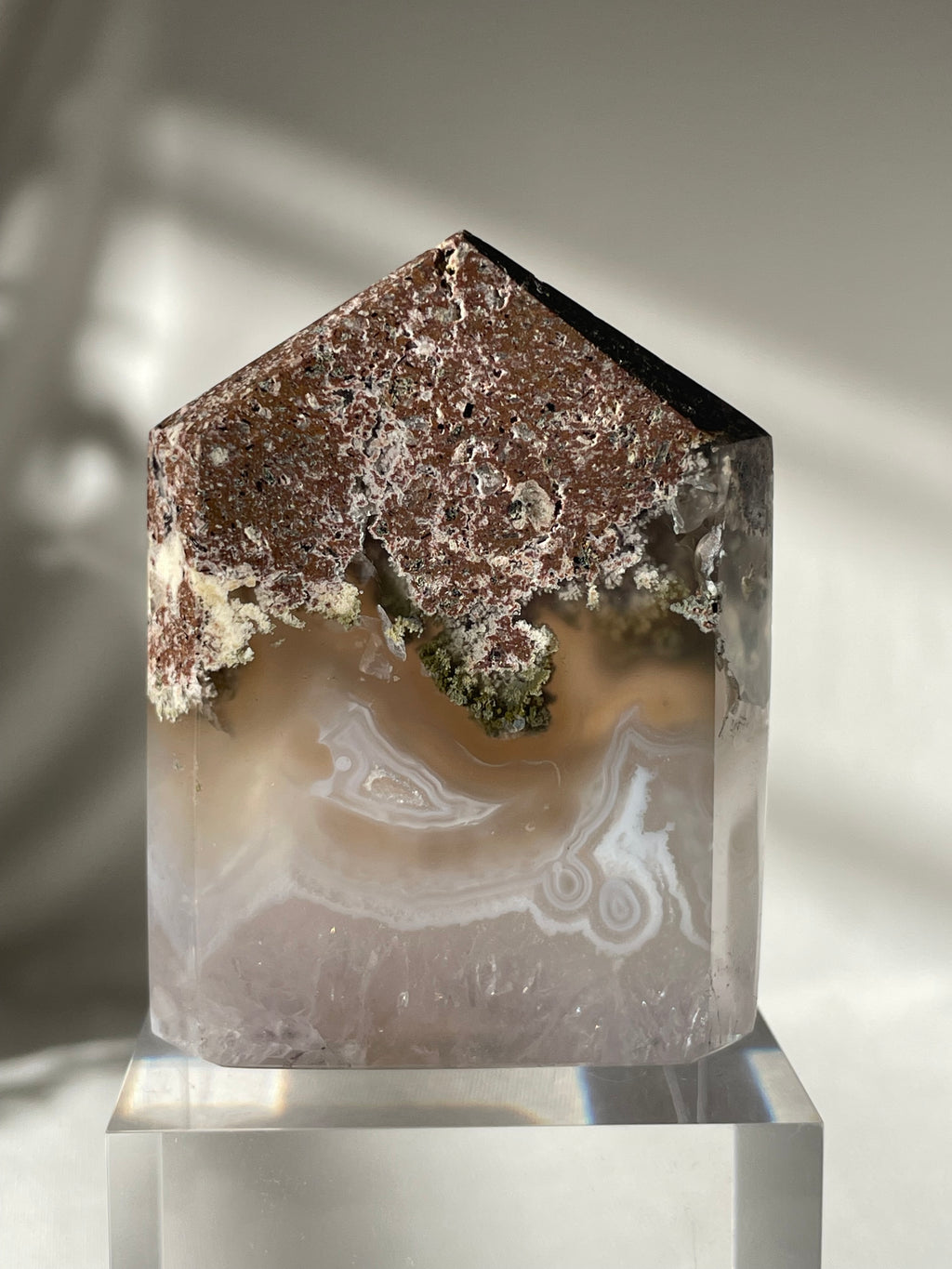 Scenic moss agate tower with earthy tones and unique patterns, displayed on a clear pedestal.