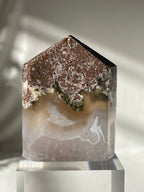 Scenic moss agate tower with earthy tones and unique patterns, displayed on a clear pedestal.