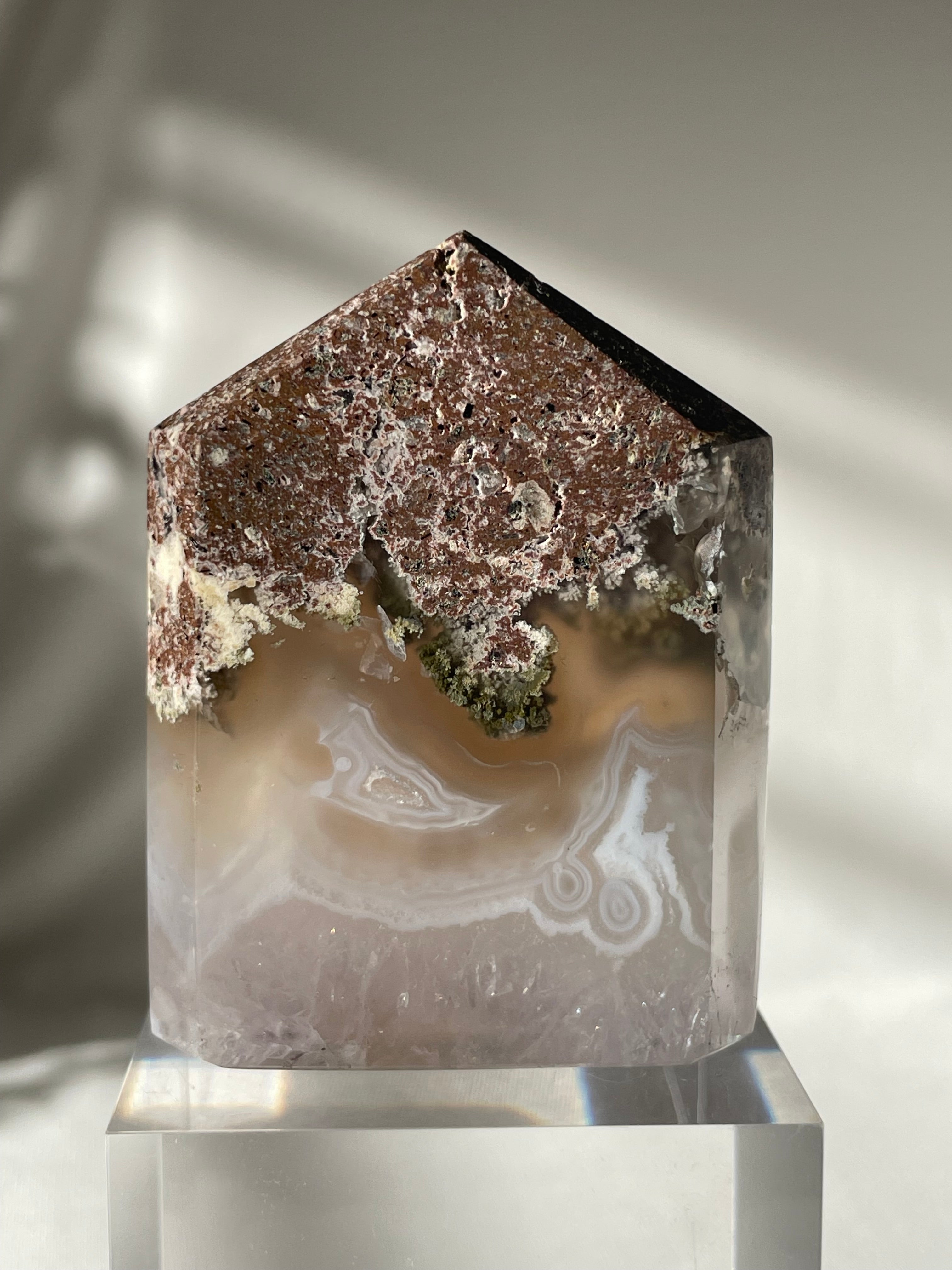 Scenic moss agate tower with earthy tones and unique patterns, displayed on a clear pedestal.