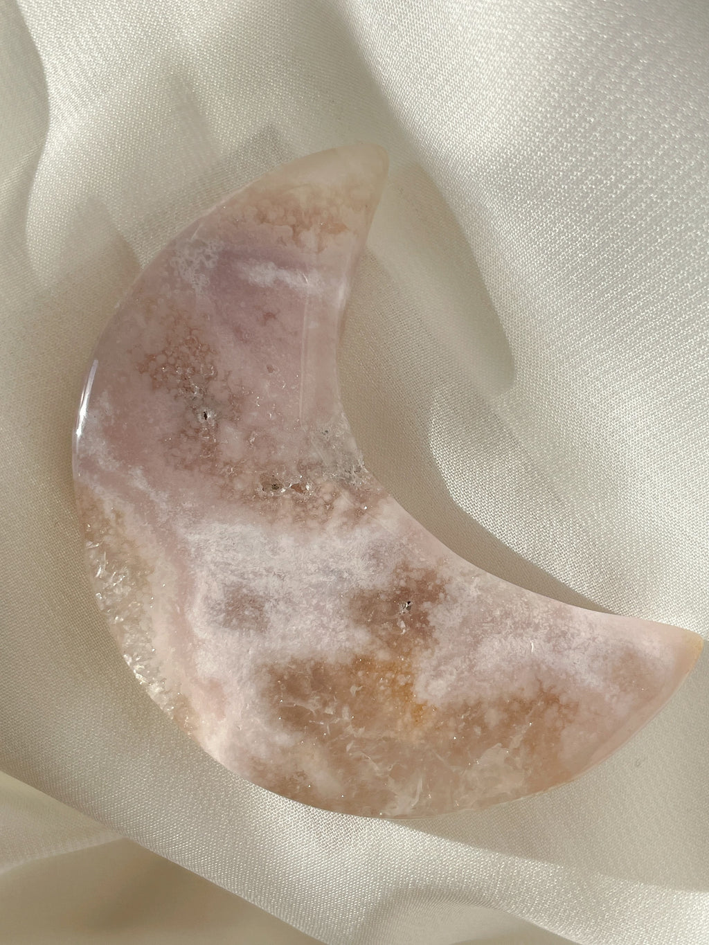 Beautiful flower agate moon with soft pink hues, resting on a light fabric background.