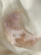 Beautiful flower agate moon with soft pink hues, resting on a light fabric background.
