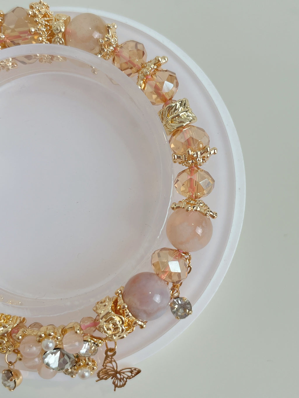 A delicate butterfly bracelet featuring flower agate and sparkling crystal beads, elegantly displayed on a circular stand.